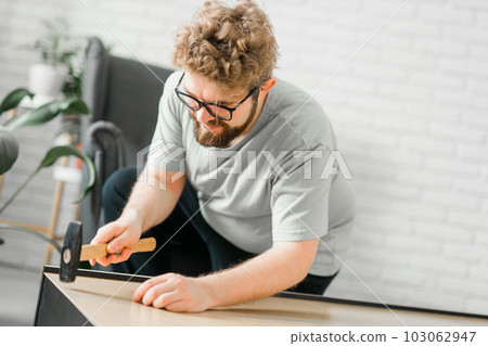 Bearded millennial man assemble his bookcase. He uses tools for furniture. Furniture for the interior room or apartments Bearded millennial man assemble his bookcase. He uses tools for furniture. Furniture for the interior room or apartments 103062947