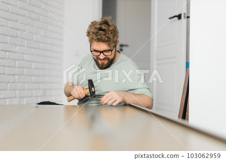 Young attractive man assembles furniture - handwerker and interior objects concept Young attractive man assembles furniture - handwerker and interior objects concept 103062959