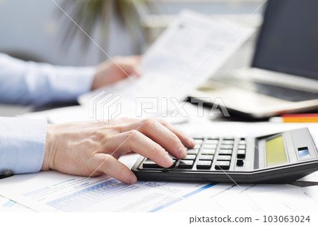Businessman using calculator to calculate bills at the table in office Businessman using calculator to calculate bills at the table in office 103063024