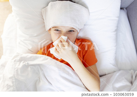 Sick child boy is lying in bed with high fever and blowing his nose 103063059