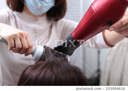 Drying long brown hair with hair dryer and a round brush. Close-up. Drying long brown hair with hair dryer and a round brush. Close-up. 103064616