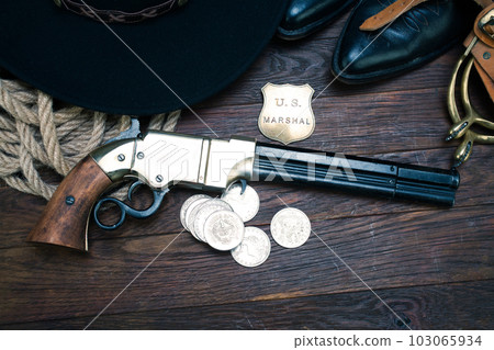 Old West gun with U.S. Marshal badge and silver dollars with hat, rope and cowboy boots 103065934