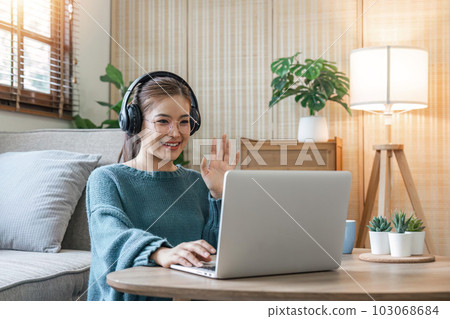 Young happy smiling woman in casual clothes sitting on sofa work online talk by video call with laptop pc computer wave hand rest relax indoors at home People lifestyle leisure concept Young happy smiling woman in casual clothes sitting on sofa work online talk by video call with laptop pc computer wave hand rest relax indoors at home People lifestyle leisure concept 103068684
