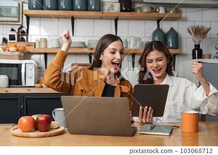 Two happy teenage girls Glad to raise your hand to receive message on tablet resting in kitchen 103068712