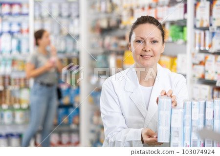 Adult female pharmacist arranges products in pharmacy 103074924