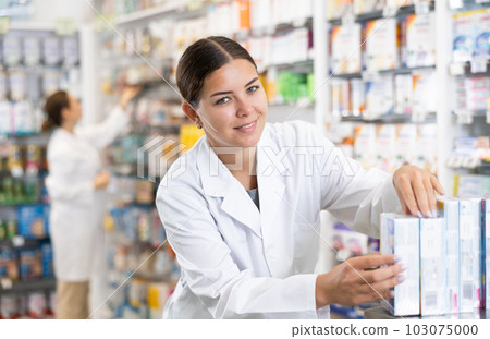 Young female pharmacist arranges product in pharmacy Young female pharmacist arranges product in pharmacy 103075000