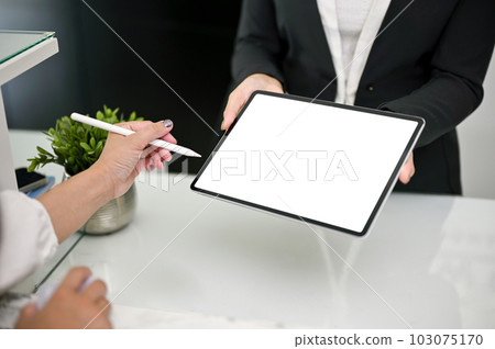 Close-up image of a receptionist is handing a digital tablet to a customer to sign 103075170