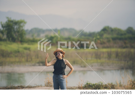 beautiful asian woman standing on open land scape and  raising right thumb with good feeling 103075565