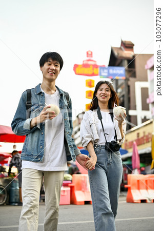 Young Asian tourist couple holding hands enjoys walking around Chiang Mai's Chinatown 103077296