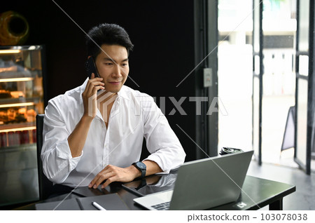An Asian businessman talking on the phone with his business client in a coffee shop. 103078038