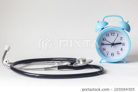 On a white background, a blue alarm clock with a stethoscope near On a white background, a blue alarm clock with a stethoscope near 103084305