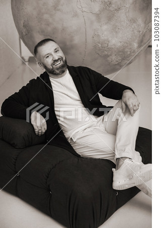 happy smiling man sitting in an armchair in the interior 103087394
