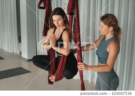 The coach corrects the girl's back in a hanging hammock. Fly yoga in the gym The coach corrects the girl's back in a hanging hammock. Fly yoga in the gym 103087536