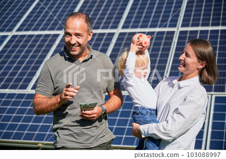 Modern family investing into their son. Man, his wife and little son joy about money they saved by buying solar panels. Concept of saving money, investment in renewable energy. 103088997