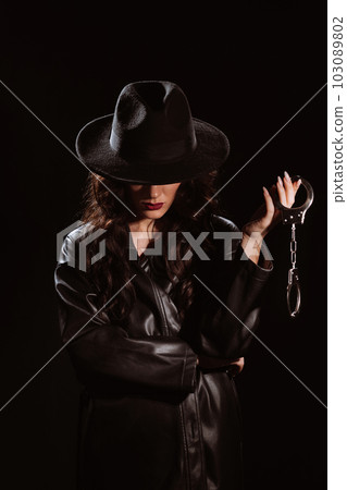 woman in a leather raincoat and hat with police handcuffs for BDSM sex 103089802