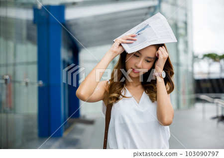 An Asian woman uses a newspaper to cover her face, feeling the damaging effects of city pollution and sun exposure on her skin and health. An Asian woman uses a newspaper to cover her face, feeling the damaging effects of city pollution and sun exposure on her skin and health. 103090797