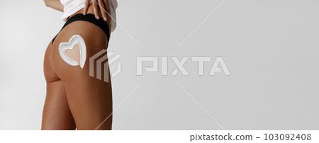 Cropped image of female tanned body, buttocks with sunscreen on body. Model posing in underwear against white background Cropped image of female tanned body, buttocks with sunscreen on body. Model posing in underwear against white background 103092408