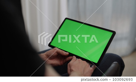 Man sitting indoors on a chair with tablet pc with green screen 103092693