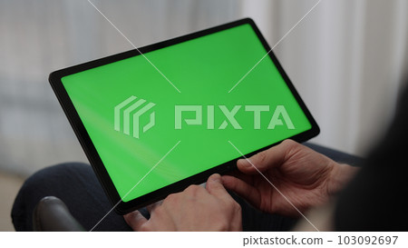 Man sitting indoors on a chair with tablet pc with green screen 103092697
