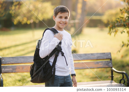 Schoolboy go to school in the morning. Happy teenager in white shirt with black backpack go to study Schoolboy go to school in the morning. Happy teenager in white shirt with black backpack go to study 103093314