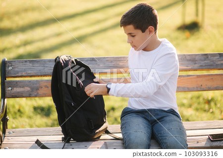 Handsome teenage boy take from his backpack powerbark for charging smarphone. Cute boy in the park in autumn time Handsome teenage boy take from his backpack powerbark for charging smarphone. Cute boy in the park in autumn time 103093316