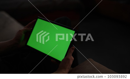 Man at home lying on a couch with tablet pc with green screen 103093892