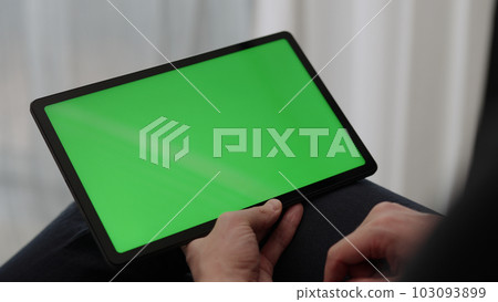 Man sitting indoors on a chair with tablet pc with green screen 103093899