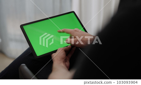 Man sitting indoors on a chair with tablet pc with green screen 103093904
