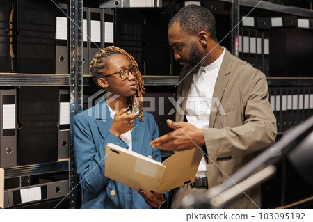 African american detective reading and discussing criminal case file. Man and woman investigators analyzing witness statement and forensic expertise in police report together African american detective reading and discussing criminal case file. Man and woman investigators analyzing witness statement and forensic expertise in police report together 103095192