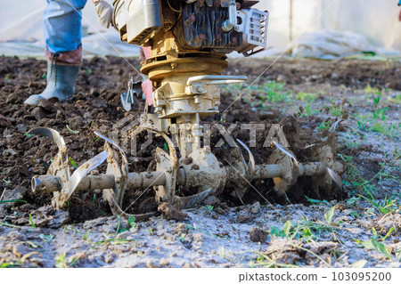 There is farmer plowing ground with tiller block using motor cultivator in garden 103095200