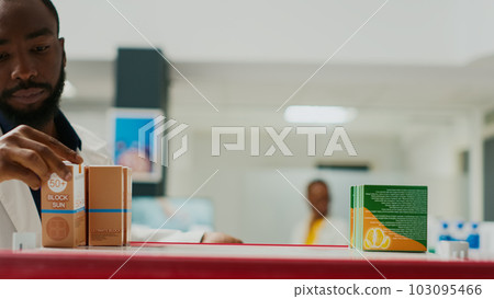 Pharmacy worker organizing products on shelves, arranging medicaments and supplements. Young man putting medicine and vitamins on pharmaceutical racks, medical retail store. Tripod shot. Close up. 103095466