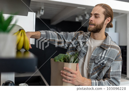 Man unpacking vegetables and fruits in kitchen after vising store, buying fresh products. Man unpacking vegetables and fruits in kitchen after vising store, buying fresh products. 103096228