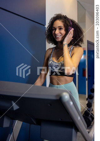 Curly-haired young woman on a treadmill looking contented Curly-haired young woman on a treadmill looking contented 103096403