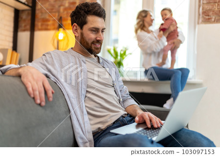 Father working on laptop, mother and daughter on background playing. 103097153