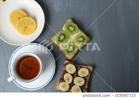 breakfast, tea with lemon and sandwiches, bread with chocolate, banana and kiwi slices on a gray background with space for text breakfast, tea with lemon and sandwiches, bread with chocolate, banana and kiwi slices on a gray background with space for text 103097723