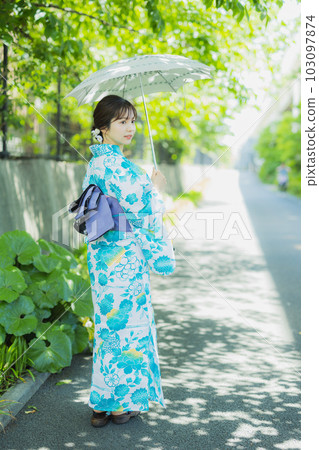 A woman in a yukata walking outdoors with a parasol 103097874