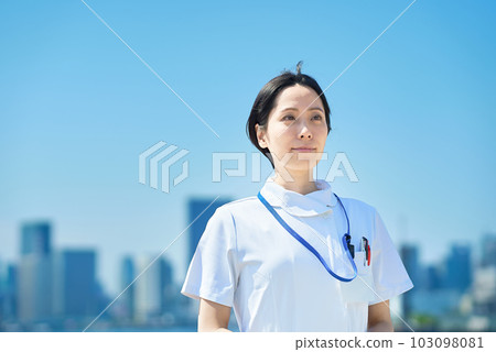 一位身穿白大衣的女士站在陽光明媚的城市景觀前 103098081