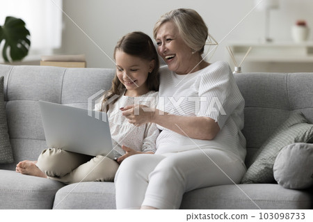 Happy granny and grandchild resting on sofa with notebook Happy granny and grandchild resting on sofa with notebook 103098733