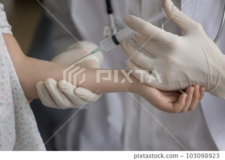Unrecognizable nurse holds syringe makes injection to little girl, closeup Unrecognizable nurse holds syringe makes injection to little girl, closeup 103098923
