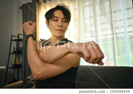 Handsome muscular man in sportswear stretching his arms, warming up exercises before working out at home 103099449