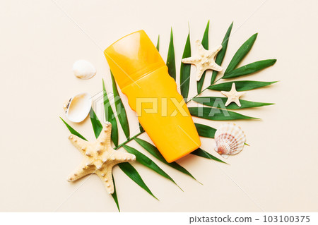 Sunscreen spray bottle. Bottle with sun protection cream and sea shells with tropical green leaf on color background, top view 103100375