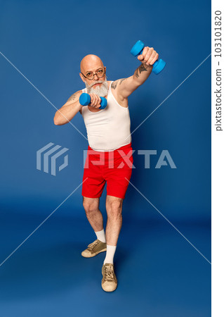 Portrait of mature, bearded man in sportswear training with dumbbells against blue studio background Portrait of mature, bearded man in sportswear training with dumbbells against blue studio background 103101820