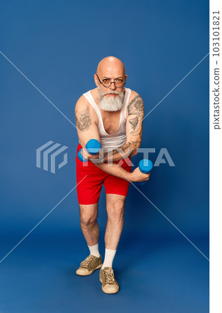 Portrait of mature, bearded man in sportswear training with dumbbells against blue studio background 103101821