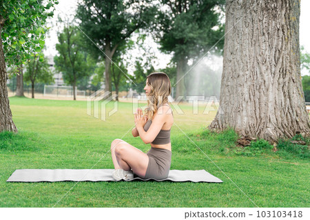 Young fit blond woman sitting in lotus yoga pose with hands as in prayer in park Young fit blond woman sitting in lotus yoga pose with hands as in prayer in park 103103418