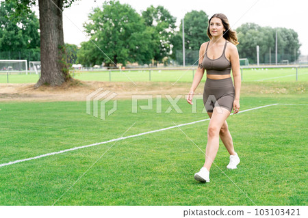 Caucasian young woman in fitness clothes and sneakers walking on football field Caucasian young woman in fitness clothes and sneakers walking on football field 103103421