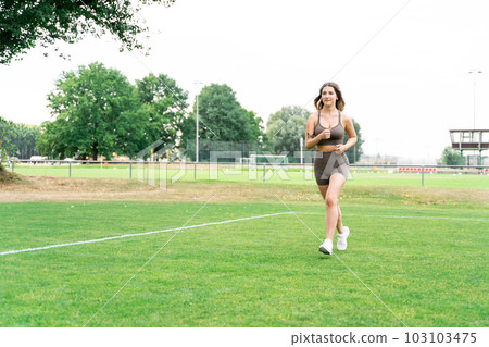 Blond young woman in fitness clothes and sneakers jogging on football field Blond young woman in fitness clothes and sneakers jogging on football field 103103475