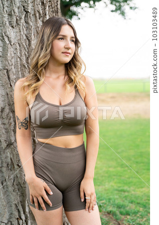 Caucasian woman in fitness clothes standing in front of tree trunk and posing 103103489