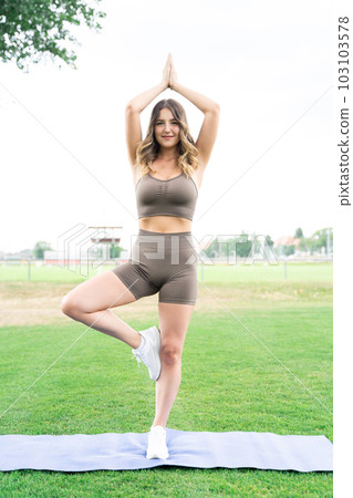 Young blond woman standing in yoga pose on one leg with hands up as in prayer Young blond woman standing in yoga pose on one leg with hands up as in prayer 103103578