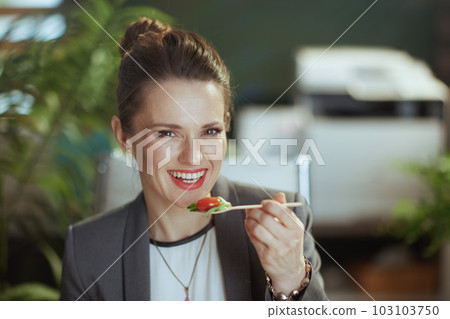 smiling business woman in green office eating salad 103103750