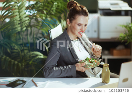 smiling business owner woman in green office eating salad 103103756